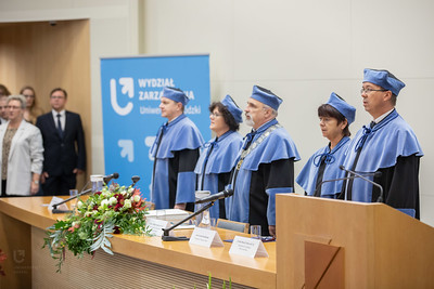 kolegium dziekańskie wydziału zarządzania w togach na tle roll-upa za stołem prezydialnym