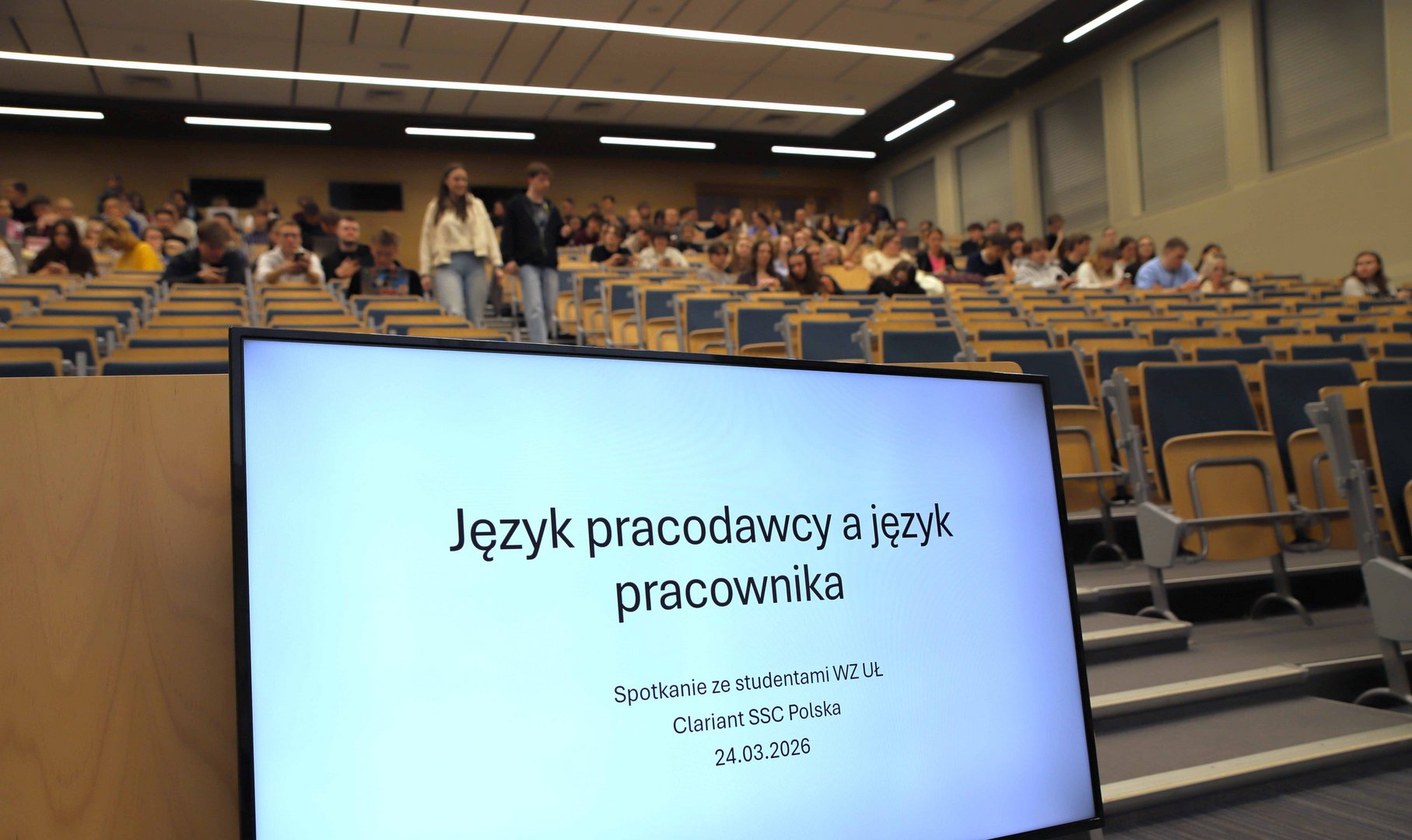 tytuł wykładu na ekranie monitora i widok na aulę