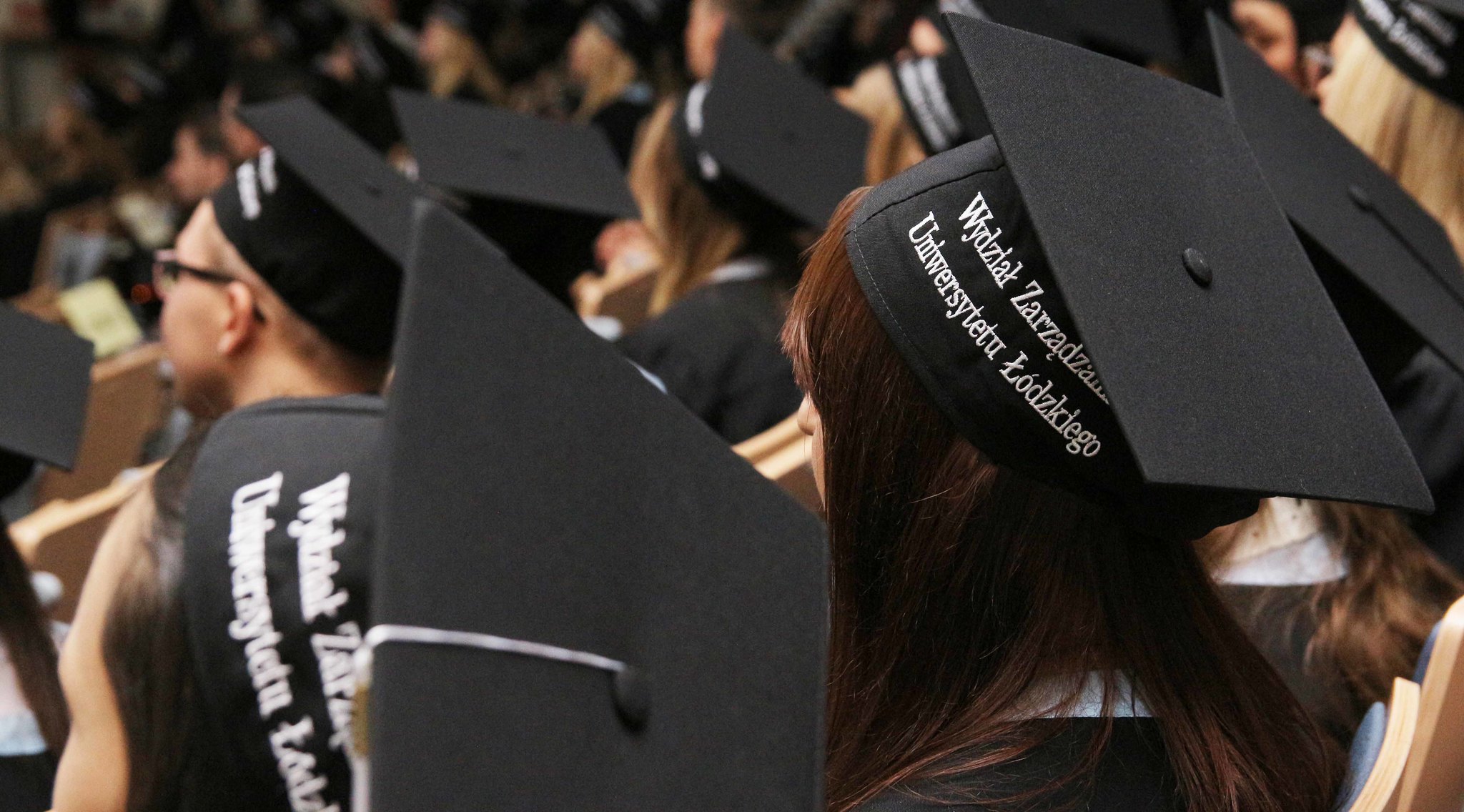 dwa birety osób siedzących na auli, w tle inne osoby