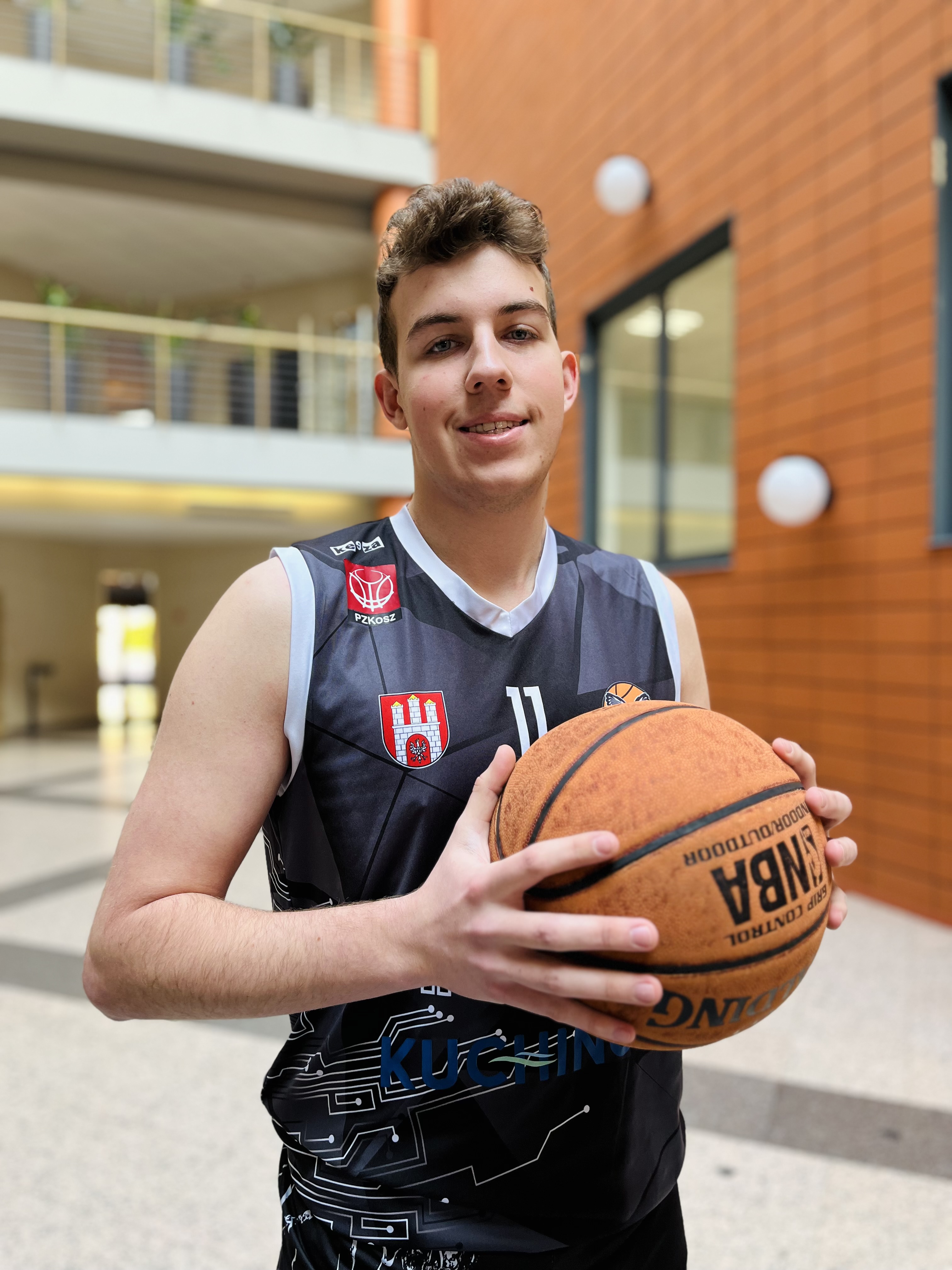 Zdjęcie przedstawia mężczyznę z piłką do koszykówki, stojącego na patio Wydziału