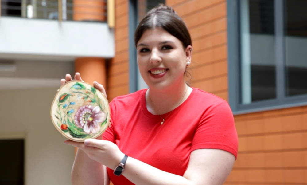 Zdjęcie przedstawia kobietę z obrazkiem namalowanym na drewienku