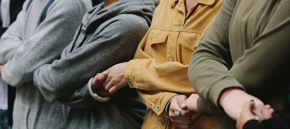 Osoby stojące obok siebie i trzymające się za skrzyżowane ręce