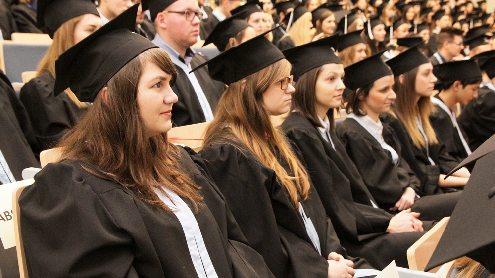 absolwenci siedzą w rzędach na auli w togach i biretach