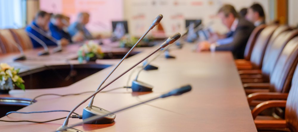 stół prezydialny na nim mikrofony przy nim siedzący ludzie