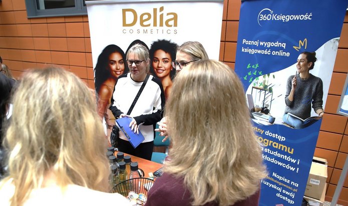 uczestnicy wydarzenia na stoisku na tle roll-upów firm