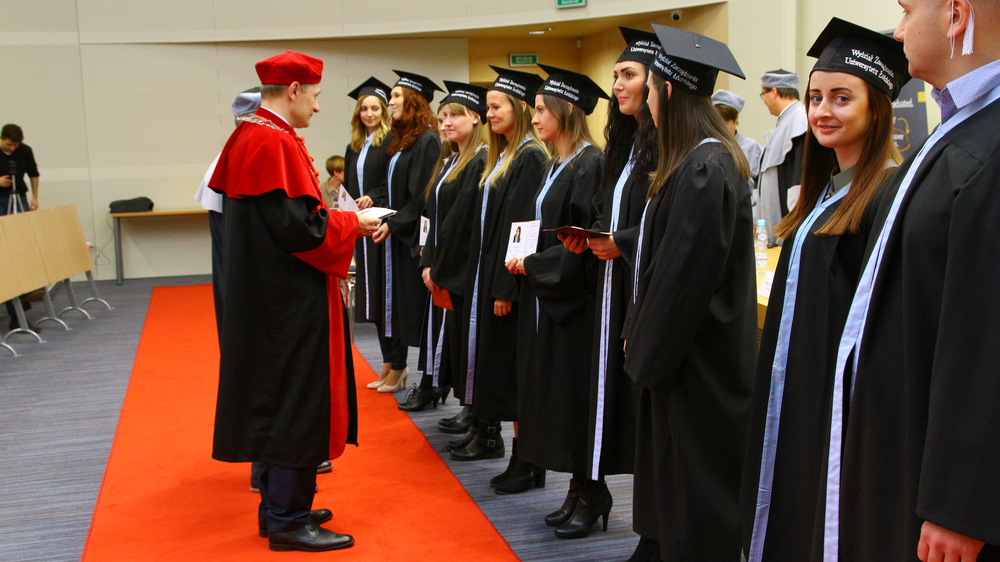 Prorektor i Dziekan wręczają dyplomy najlepszym absolwentom, absolwenci stoją w rzędzie