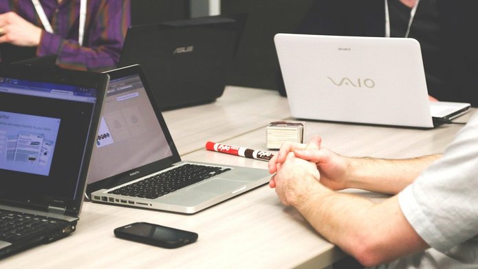 Widok na biurko z otwartymi laptopami, widoczna osoba z boku