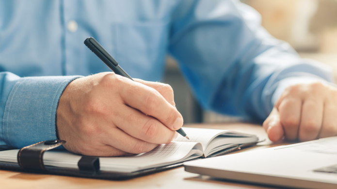 Zdjęcie przedstawia dłoń notującą w notatniku
