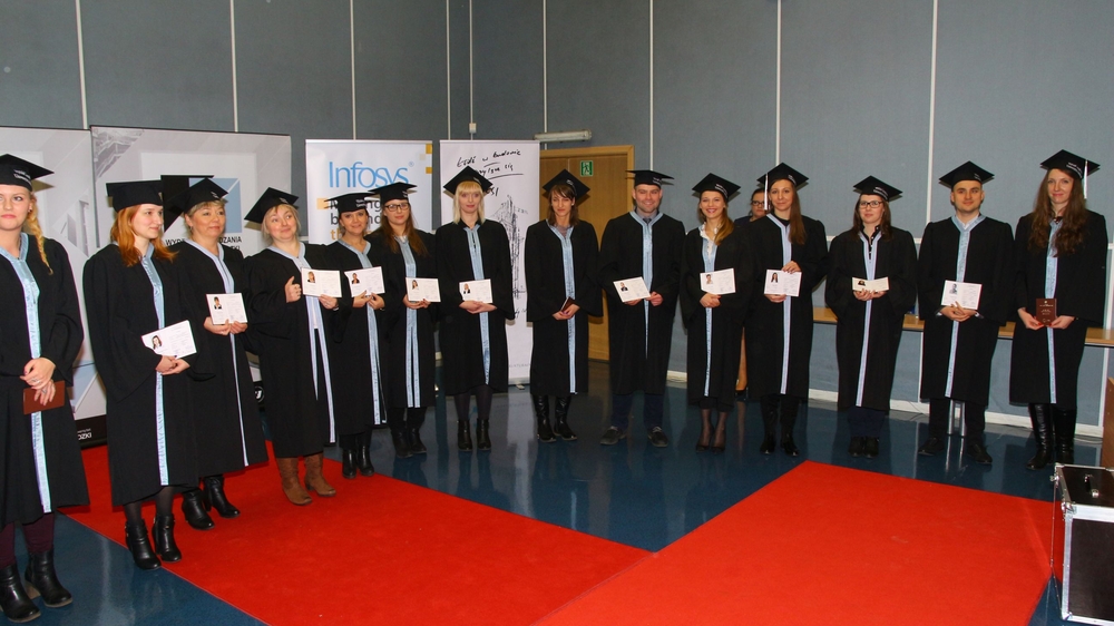 absolwenci w rzędzie stoją na auli z odebranymi dyplomami