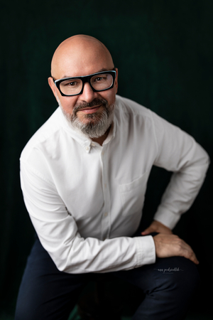 mężczyzna na czarnym tle w okularach uśmiecha się 