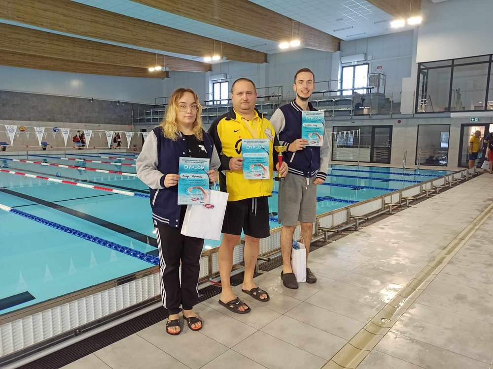 Studenci UŁ, Kinga Wychorska i Łukasz Gmaj, nagrodzeni dyplomami stoją na pływalni z trenerem Piotrem Jaworowiczem