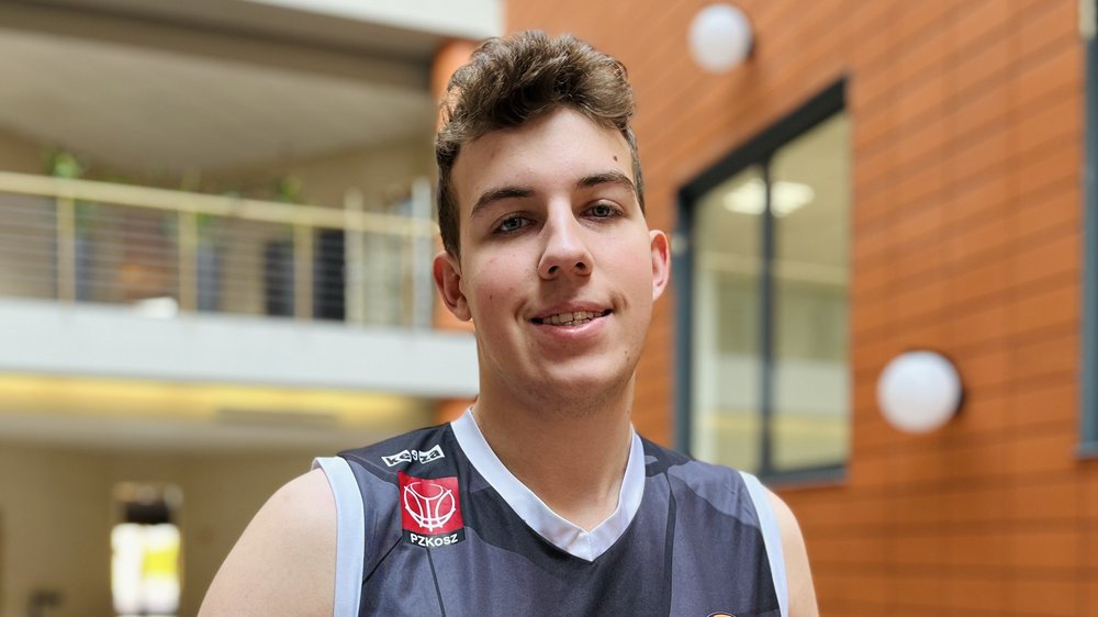 Zdjęcie przedstawia mężczyznę z piłką do koszykówki, stojącego na patio Wydziału