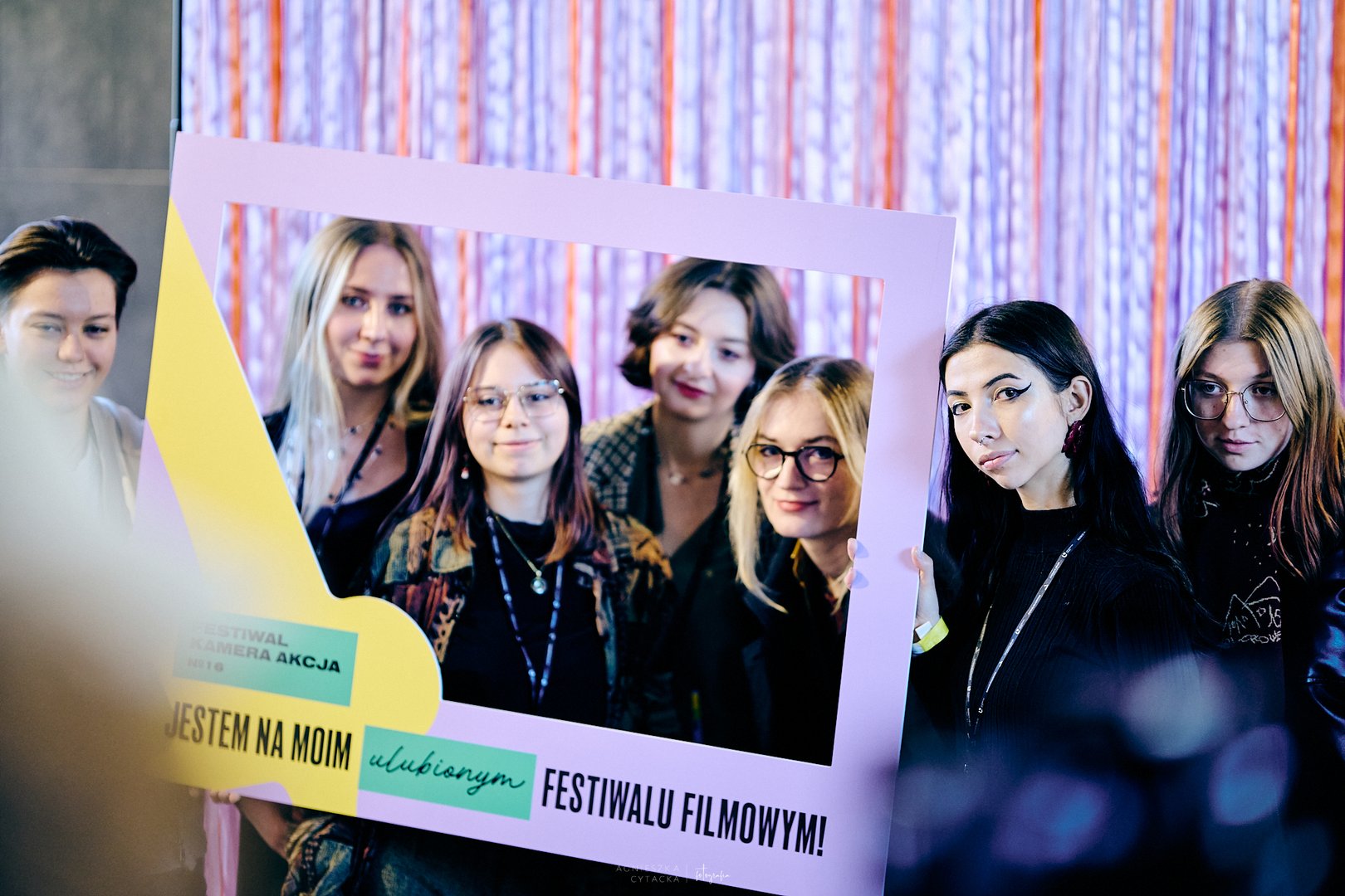 A group of young people poses for a photo with a promotional frame for the Camera Action Festival.